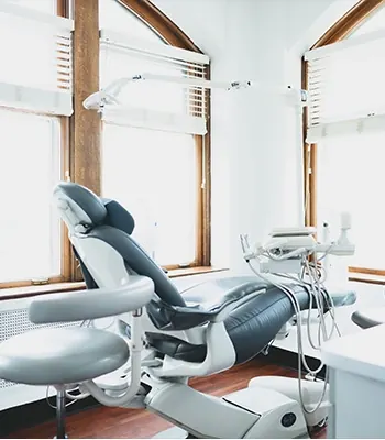 A treatment room with a modern dental chair between two tall wooden-framed windows.