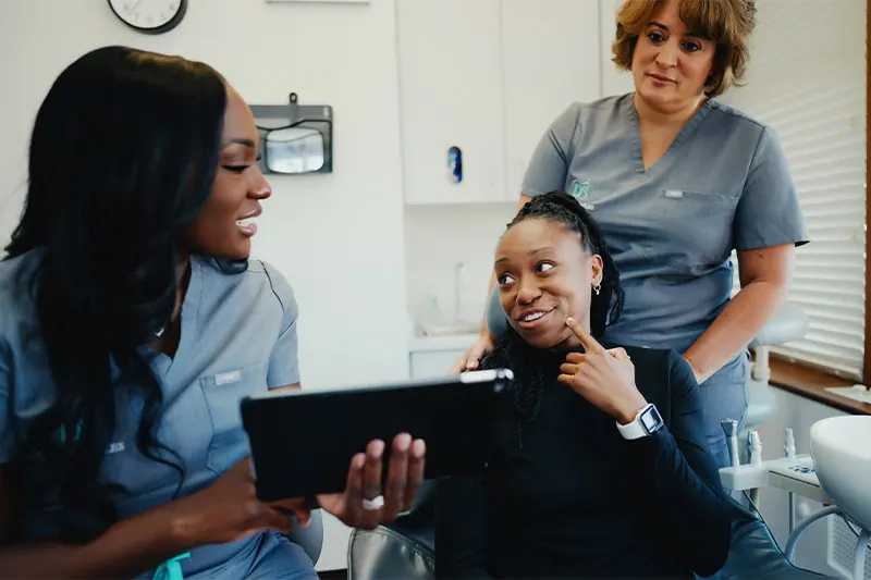 A team member showing a seated patient images on a tablet while a colleague looks on.